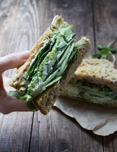 a person is holding a sandwich with avocado and spinach in it on wax paper