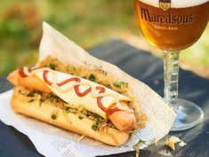 a hot dog with mustard and ketchup on a napkin next to a glass of beer