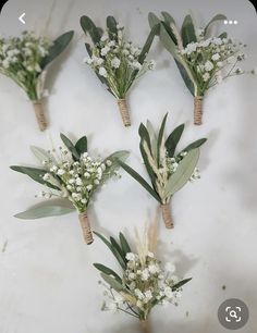 six boutonnieres with white flowers and greenery are arranged on a table