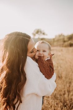 a woman holding a baby in her arms and smiling at the camera while standing in a field