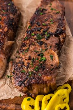 two pieces of meat sitting on top of a piece of wax paper next to yellow peppers