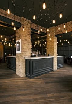 a bar with lights hanging from the ceiling in a room that has dark wood floors and exposed brick walls