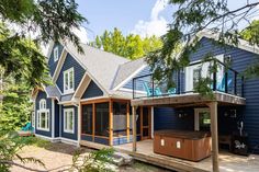 a blue house with a hot tub on the deck and trees in front of it