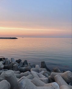 there is a bench sitting on the rocks by the water's edge at sunset