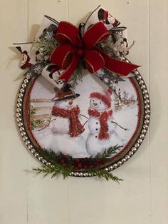 a christmas ornament hanging on the side of a wall with two snowmen