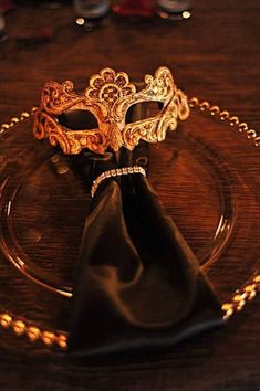 a fancy mask on a glass plate with a black napkin and gold chain around it