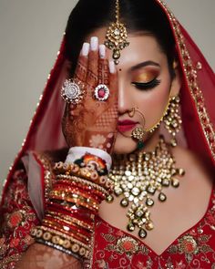 a woman in red and gold is holding her hands up to her face while wearing jewelry