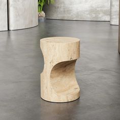 a wooden stool sitting on top of a cement floor next to a potted plant