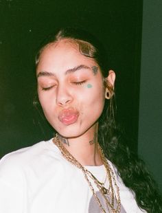 a young woman with her eyes closed and tongue out, making a funny face while wearing gold jewelry