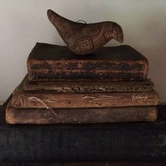 three old books stacked on top of each other with a wooden bird sitting on them