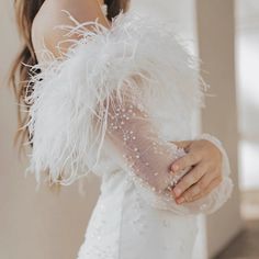 a woman in a white dress with feathers on her arm and hand, wearing a veil