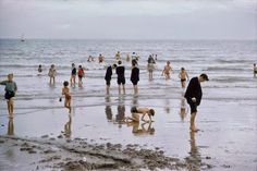 many people are on the beach playing in the water and sand while others walk around