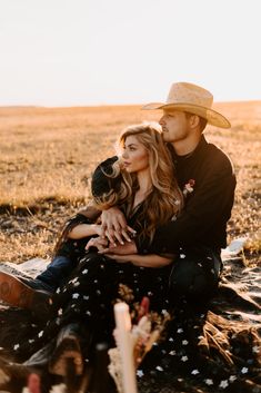 a man and woman are sitting on the ground with their arms around each other while holding hands