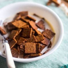 a white bowl filled with brown sugar cubes next to a spoon on top of a blue table cloth