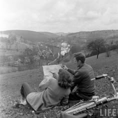 black and white photograph of two people sitting on the ground looking at something in front of them