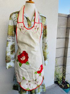 a white apron with red flowers on it sitting on top of a wooden table next to a potted plant