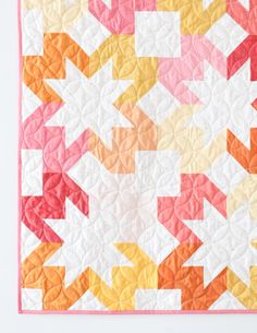 an orange, yellow and pink quilt on a white surface with arrows in the center