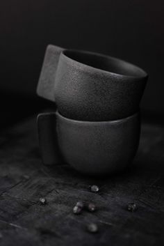 two black cups sitting next to each other on a wooden table with scattered seeds around them