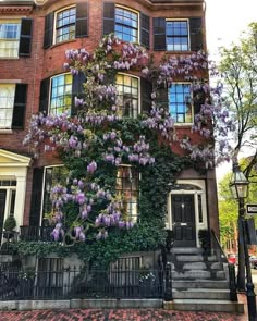 a large brick building with purple flowers growing on it's side and stairs leading up to the front door