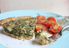 a piece of quiche with spinach and tomatoes on a plate next to a fork