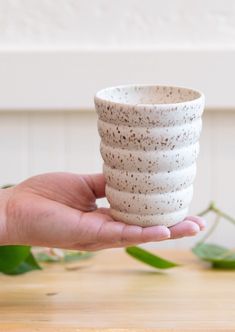 a hand holding a white cup on top of a wooden table