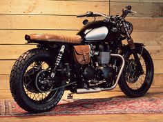 a black motorcycle parked on top of a wooden floor next to a rug and wall