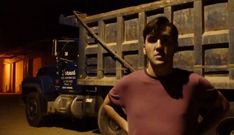 a man standing in front of a dump truck at night with his hand on the wheel