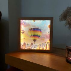 a colorful hot air balloon floating in the sky with mountains and clouds behind it on a wooden table