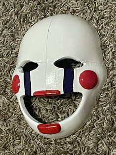 a white mask with red and blue stripes on it's face is laying on the carpet