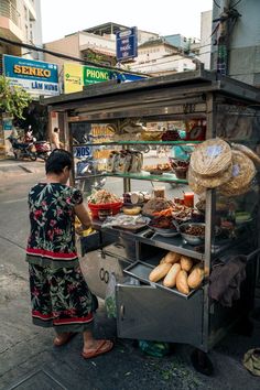 a woman standing in front of a food cart on the side of a city street