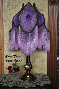 a purple lamp with tassels on it sitting on a table next to a vase