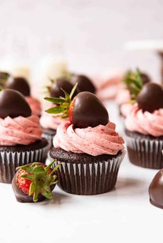 chocolate cupcakes with pink frosting and strawberries on top, ready to be eaten