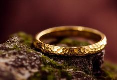 a gold wedding band sitting on top of a moss covered rock