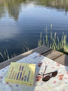 a book and sunglasses sitting on top of a table next to a body of water