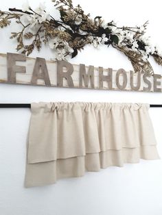 a sign that says farmhouse hangs on the wall next to a ruffled valance