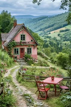 a small pink house in the middle of a lush green hillside with trees and flowers