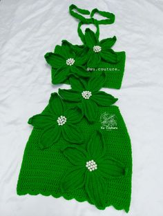 a green crocheted dress with flowers on the neck and side, sitting on a white sheet