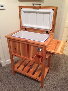 an open wooden cooler sitting on top of a floor next to a table and chair