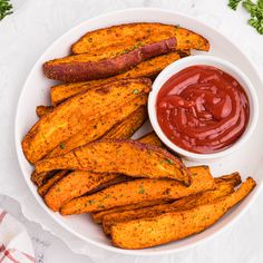 baked sweet potato wedges with ketchup and parsley on the side in a white bowl