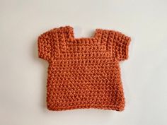 an orange crocheted sweater laying on top of a white surface