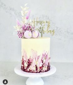 a white cake with pink flowers on top and happy birthday written on the side in gold lettering