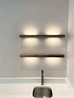 a sink and some shelves with lights above it in a room that has white walls