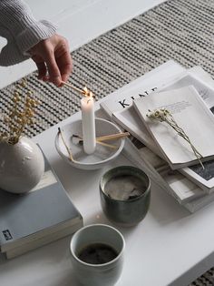 a person lighting a candle on top of a coffee table with books and cups next to it