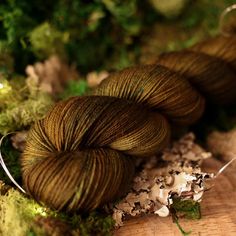 two skeins of yarn sitting on top of a wooden table next to moss