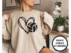 a woman sitting on top of a bed wearing a sweater with a volleyball ball in the shape of a heart