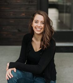 a smiling woman sitting on the ground in front of a wooden door with her arms crossed