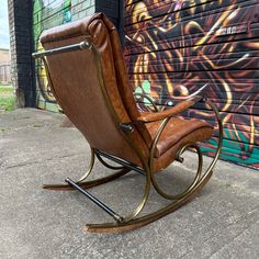 a brown leather rocking chair sitting in front of a graffiti covered wall