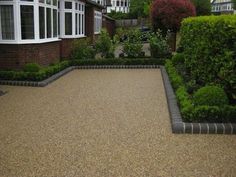 a graveled area in front of a house with hedges and shrubs around it,