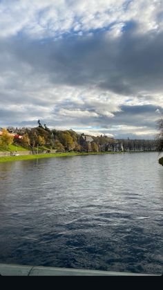 a body of water with trees in the background and clouds in the sky above it