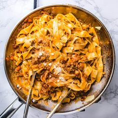 a skillet filled with pasta and meat on top of a marble countertop next to utensils